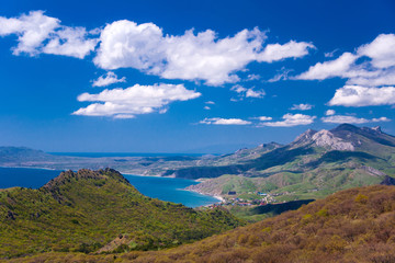 view from the mountains to the seashore with clouds in the blue sky