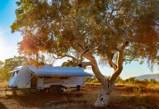 Large caravan and four wheel drive vehicle camped next to a gum tree in the Karijini National Park, Australia in the late afternoon sun.