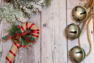 Jingle bells on rope with decorative flocked snow pine branches and a burlap candy cane. Wood background, copy space included
