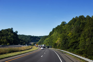 Cars and trucks drive along a beautiful scenic highway among mountains and hills on a sunny summer...