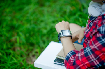 The girl watches the watch in hand, watches the time in a black watch, wears a red shirt and a green background. And there is a copy space.