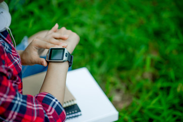 The girl watches the watch in hand, watches the time in a black watch, wears a red shirt and a green background. And there is a copy space.