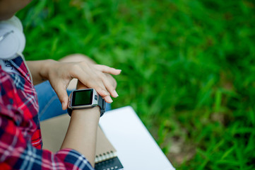 The girl watches the watch in hand, watches the time in a black watch, wears a red shirt and a green background. And there is a copy space.