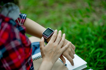 The girl watches the watch in hand, watches the time in a black watch, wears a red shirt and a green background. And there is a copy space.