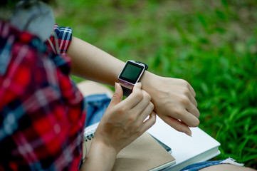 The girl watches the watch in hand, watches the time in a black watch, wears a red shirt and a green background. And there is a copy space.