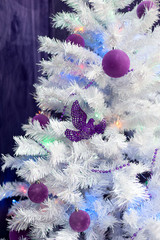 Christmas background. White Christmas fir tree with purple Christmas decorations on a purple background
