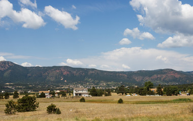 Scenic mountains, clear deep sky with white clouds on a summer sunny day. At the foot of the mountains are located houses of small American cities. Colorado, USA.