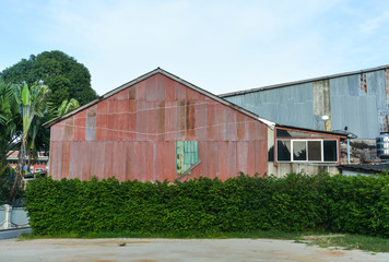 Fototapeta na wymiar old pink galvanized sheet (zinc sheet) building with green tree bush fence