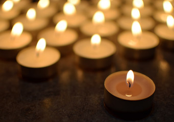 Fototapeta na wymiar Round tea light candles burning in darkness. Advent or memorial prayer candle flame.
