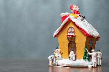 Miniature people painting house and Santa Claus sitting on the roof