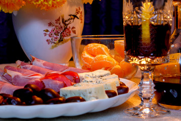 Beautiful composition with food, drink and flowers. Cheese, ham, olives, liquor, flowers, old candle holder, mandarins and lemon.