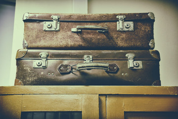 Two old vintage suitcases with handles lie in the dust on the wardrobe