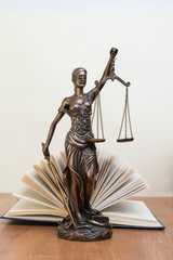 statue of justice on wooden table against the background of an open book