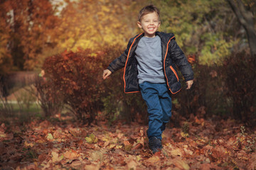 Handsome cheerful guy runs in the park on fallen leaves and rejoices, laughs.