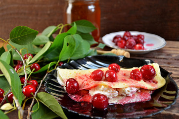 Pancakes with cheese and cherries on a black plate on a wooden background