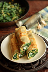 Pancakes with spinach on a wooden background. Bowl with spinach in the background