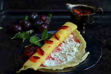 Pancake with cheese and plum jam on a black background