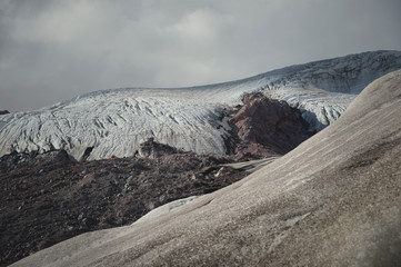 Mountain landscape dusty dirty volcanic slope with cracked melting glacier. Global warming. Glaciers of the North Caucasus