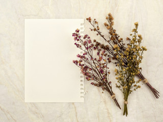 Top view of note pad paper with group of bouquet dried and wilted multiple color Gypsophila flowers on matt marble background for text, letter, message or verse