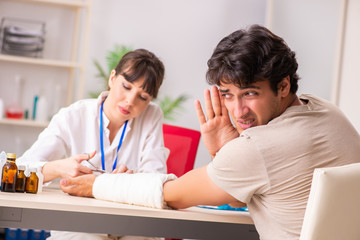 Young man with bandaged arm visiting female doctor traumatologis