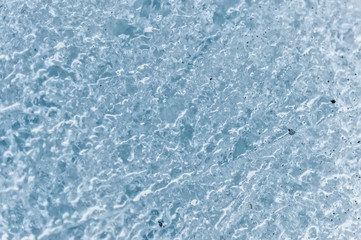 Obraz premium A close-up of the surface of a fragment of a glacier with a structure of strips and bubbles interspersed with sand and rocky rock. Ice blue texture to the light. Small DOF