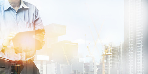 Engineer standing using tablet control and manage work at construction site.