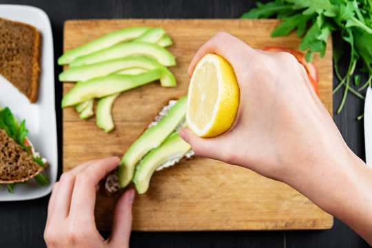 Making raw food snack. Female hands squeeze lemon juice onto avocado sandwich, top view shot - Powered by Adobe