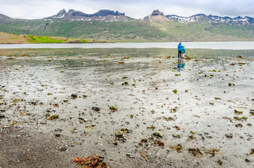 Two children watch the sea at low tide from the black beach of an Icelandic fjord