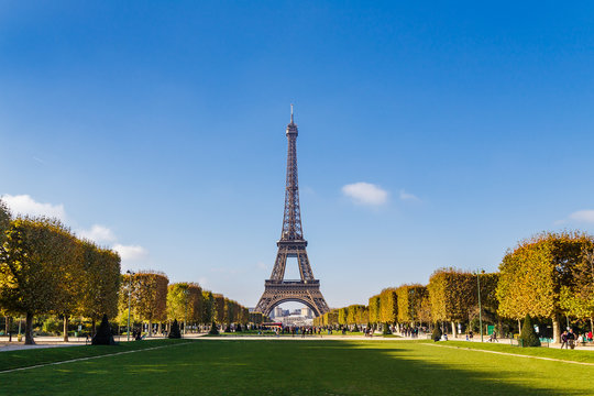 Wide shot of the Eiffel Tower in Paris seen from the lawn of the Champ de Mars one autumn day by a clear blue sky