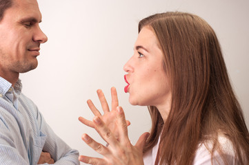 Profile of adult caucasian woman with loose hair shouting at her man who is smiling folding arms and doesn't care about the relationship shoot on white background.