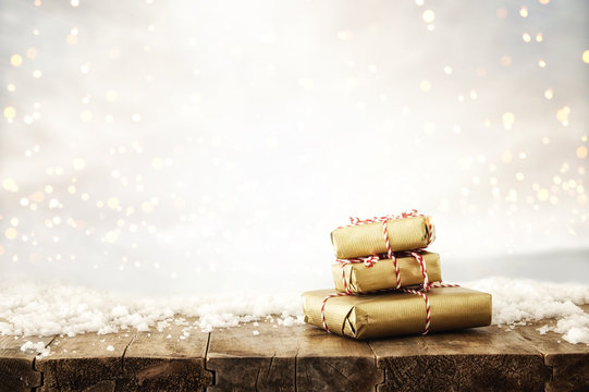 image of handmade wrapped gift boxes over wooden table covered with snow and silver glitter bokeh background.
