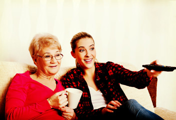 Portrait of granddaughter and grandmother sitting on couch and watching TV