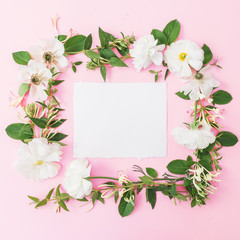 Floral frame of white flowers, buds with card on pink background. Flat lay, top view. Pastel background.