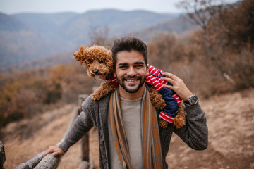 Man standing and holding dog on shoulders in nature.