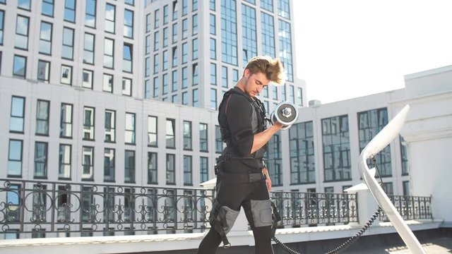 Handsome ambitious bodyduilder in EMS suit. Training on the street. Strength and power concept