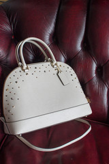 womens leather bag on a red leather sofa, leather white handbag (vertically)
