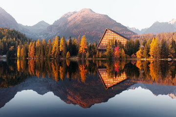 Picturesque autumn view of lake Strbske pleso in High Tatras National Park, Slovakia. Clear water with reflections of orange larch and high mountains on background. Landscape photography - obrazy, fototapety, plakaty