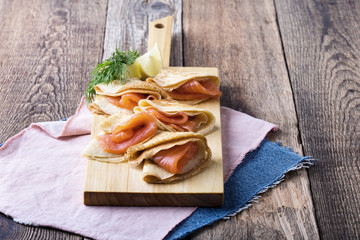 Smoked salmon appetizer, stuffed crepes on wooden board