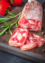 Dried sausage on a wooden board with rosemary and spices.