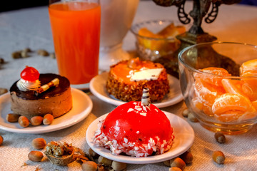 Beautiful evening composition with cakes and candle light.Old candle holder, flowers, cakes, oranges, limon, red orange juice, walnuts and hazelnuts.