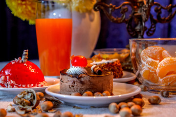 Beautiful evening composition with cakes and candle light.Old candle holder, flowers, cakes, oranges, limon, red orange juice, walnuts and hazelnuts.