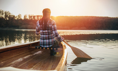 Rear view of woman canoeing on the sunset lake