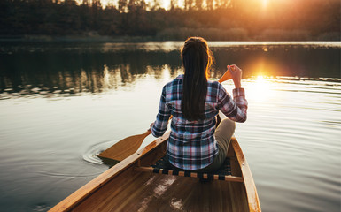 Rear view of hipster girl paddling the canoe on the sunset lake