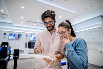 Man using tablet while woman with amazed facial expression looking at it. Tech store interior.