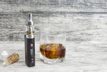 Not a full glass of alcoholic whiskey drink with an e-cigarette on a marble surface.Bad habits harmful to health 