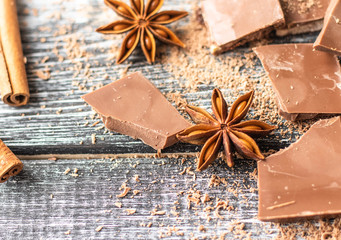 Broken chocolate pieces, cocoa powder, star anise and cinnamon on wooden background