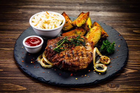 Grilled steak with baked potatoes and vegetables served on black stone plate on wooden table