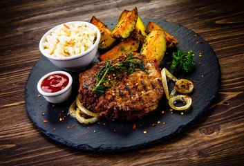 Grilled steak with baked potatoes and vegetables served on black stone plate on wooden table