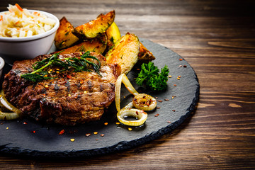 Grilled steak with baked potatoes and vegetables served on black stone plate on wooden table