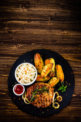 Grilled steak with baked potatoes and vegetables served on black stone plate on wooden table